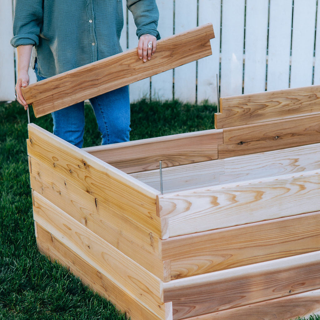 Person assembling a wooden raised garden bed outdoors.